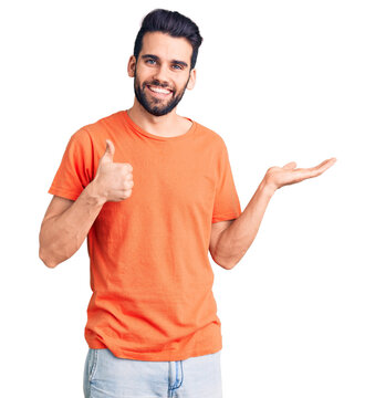 Young handsome man with beard wearing casual t-shirt showing palm hand and doing ok gesture with thumbs up, smiling happy and cheerful