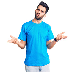 Young handsome man with beard wearing casual t-shirt clueless and confused with open arms, no idea concept.