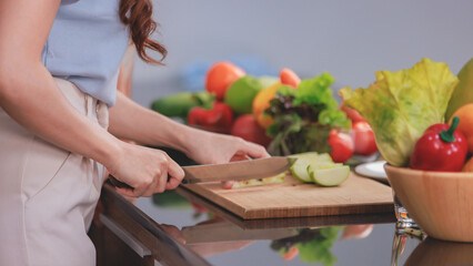 Asian young lovely couple beautiful wife at kitchen counter full of organic fresh fruits orange juice and vegetables using knife cutting green apple on chopping board while husband standing beside