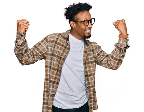 Young african american man with beard wearing casual clothes and glasses very happy and excited doing winner gesture with arms raised, smiling and screaming for success. celebration concept.