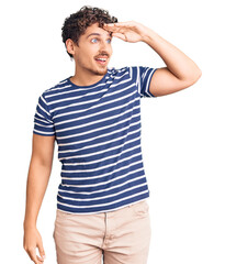 Young handsome man with curly hair wearing casual clothes very happy and smiling looking far away with hand over head. searching concept.