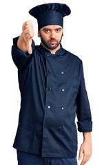 Young hispanic man wearing cooker uniform looking unhappy and angry showing rejection and negative with thumbs down gesture. bad expression.