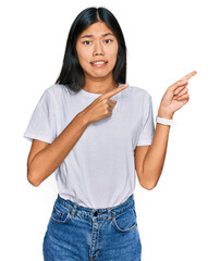 Beautiful young asian woman wearing casual white t shirt pointing aside worried and nervous with both hands, concerned and surprised expression