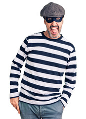 Middle age handsome man wearing burglar mask winking looking at the camera with sexy expression, cheerful and happy face.