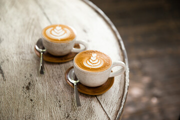 Two cups of cappuccino with latte art on saucer with spoons white wooden background