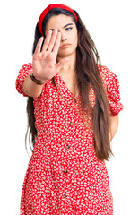 Brunette teenager girl wearing summer dress doing stop sing with palm of the hand. warning expression with negative and serious gesture on the face.