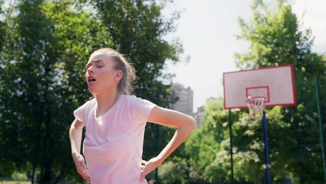 Young woman straining her back while playing basketball, feeling pain, trauma