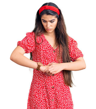 Brunette teenager girl wearing summer dress checking the time on wrist watch, relaxed and confident