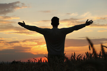 Silhouette of man with raised hands in the wheat field and sunset sky with clouds. Pavel, my silhouette and sunset. Photo was taken in the evening 5 August 2022 year, MSK time in Russia.