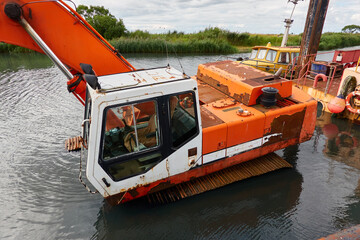 Submerged dredging excavator crane and boat in a river. Industry, special equipment, infrastructure, ecology, environmental issues, pollution concepts
