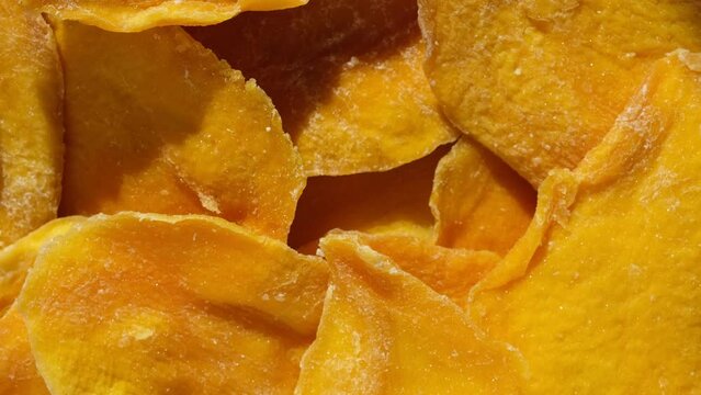 Dried mango slices close-up on a white. Top view. Closeup. Mango chips background. Dehydrated crispy fruit slices, pieces. Heap of sun-dried yellow fruit. Healthy meal. Top view, flat lay. 4K Footage.