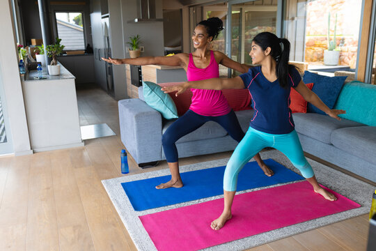 Biracial mother and daughter practicing warrior 1 pose on mats in living room