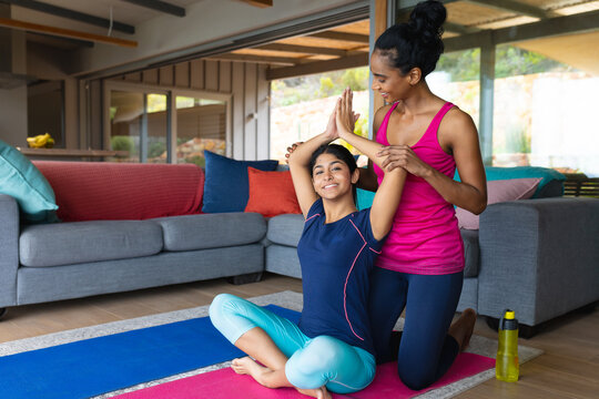 Biracial mother assisting smiling daughter in practicing yoga pose in living room