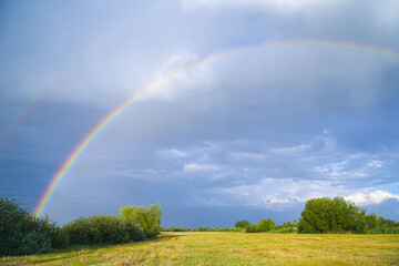 Rainbow on the background of storm clouds over a mown meadow