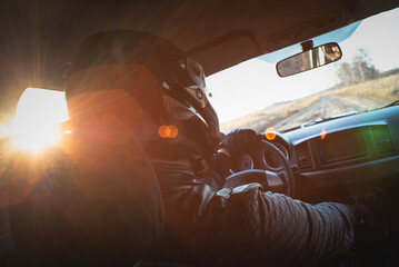 Rally car driver sitting by the steering wheel in the sunset rays concept.