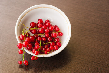 Sprigs of red currant in a white bowl closeup top view. Sweet red currant spilling out from the bowl. Currant organic berries harvest - healthy eating and food concept