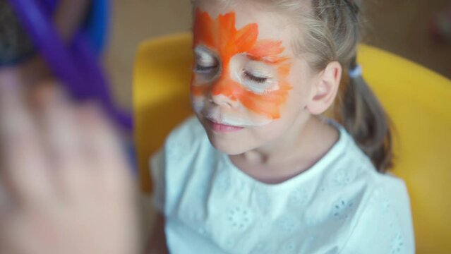Children face painting. Artist painting with brash and special body paint tiger mask on face of little girl on carnival party for children. Body art painting for childrens.