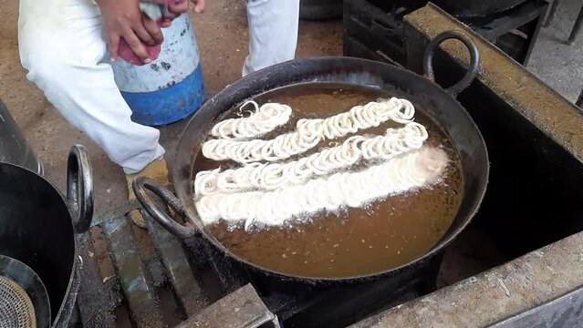 Indian male hand making Jalebi (traditional Indian fried sweet dessert) at a festival. close up shot of jalebi sweet making in a frying pan selective focus