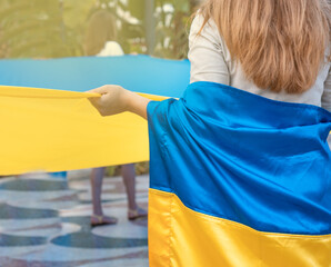 Mujer joven irreconocible en una manifestación, cogiendo la bandera de Ucrania. Fotografía horizontal con espacio para texto. - obrazy, fototapety, plakaty