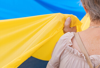 Mujer veterana cogiendo la bandera de Ucrania en una manifestación. Fotografía horizontal con espacio para texto. - obrazy, fototapety, plakaty