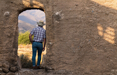 Rear view of adult man in cowboy hat and shirt standing on doorway of a backdrop building