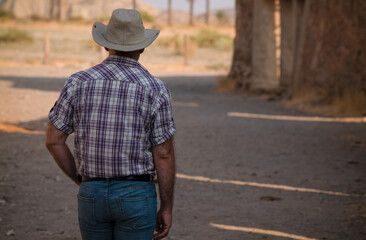 Rear view of adult man in cowboy hat and shirt against abandoned building