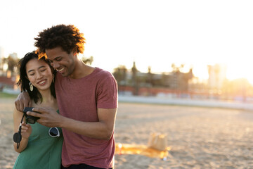 Beautiful young couple taking photos at the beach. Happy couple having fun at sea resort..