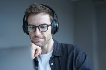 Smiling german man in headphones looking on screen of laptop and watching educational webinar