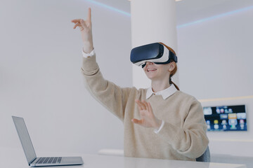 Young european woman in VR goggles in office. Student is working on futuristic design in cyberspace.
