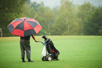 Man with colorist umbrella and electric golf cart under rain in the golf course