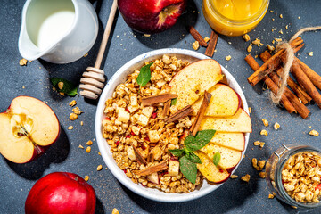 Healthy autumn breakfast granola. Apple pie granola with muesli, cinnamon spices, apples slices, honey and nuts, on black stone background copy space