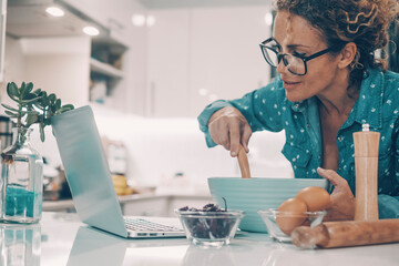 Modern wife prepare breakfast or lunch using computer and online tutorial in the kitchen at home. Real life woman cooking alone. Female people cook happy watching laptop and smiling. House lifestyle
