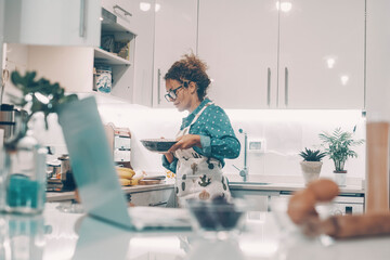 Happy woman alone at home cooking lunch with a smile. Ingredients and online computer in foreground...