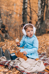 Cute little caucasian girl in a blue raincoat and fur headphones eating at a picnic in an autumn park.Autumn concept.