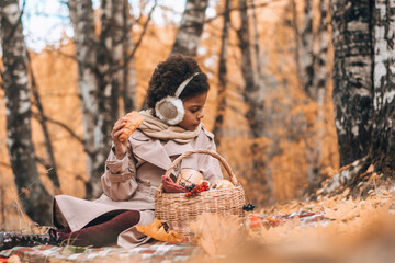 African-American girl eats a croissant at a picnic in an autumn park.Diversity,autumn concept.