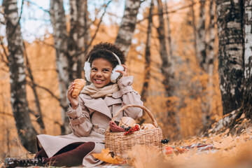 African-American girl eats a croissant at a picnic in an autumn park.Diversity,autumn concept.
