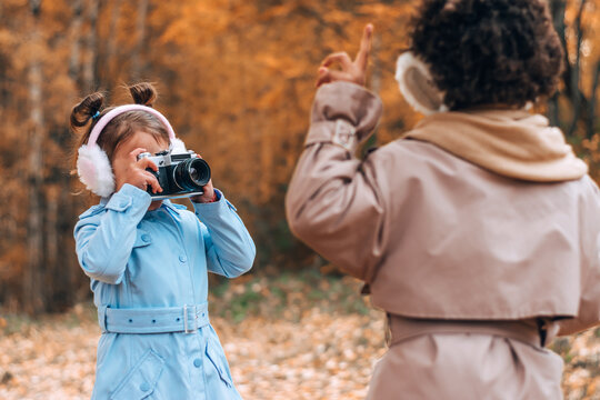 Caucasian and African-American girls take pictures of each other on camera in the autumn park.Technology,diverse people,autumnal concept.