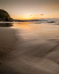 Obraz premium Sunset on a sandy beach with waves in long exposure