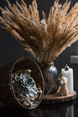 Candles, succulent, basket and a beautiful bouquet of dried pampas grass flowers in a glass vase on a dark table. An element for decoration and interior decoration.