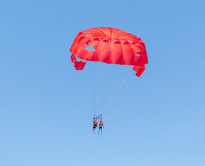 A red parachute flies in the blue sky.