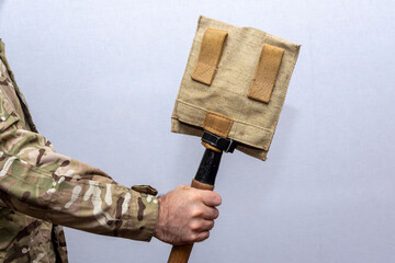 A sapper shovel in a case in the hand of a military man on a light background.