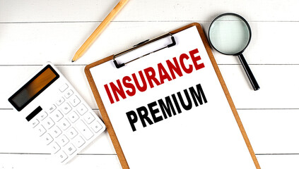 INSURANCE PREMIUM words on clipboard, with calculator, magnifier and pencil on the white wooden background
