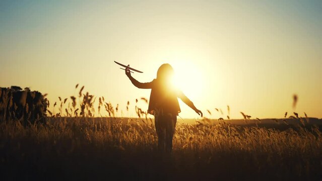 girl kid runs in the park across the field plays with a toy airplane in his hand silhouette at sunset wants an astronaut. funny fantasy children's dream concept. child runs wheat plays with a toy fun