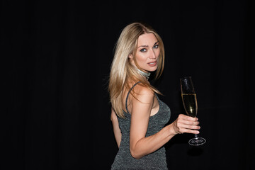 Stylish woman in dress holding glass of champagne during party isolated on black.