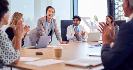 Multi-Cultural Business Team Applauding Businesswoman Leading Meeting Around Table In Modern Office