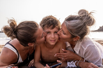 portrait of beautiful middle aged mother and her daughter kissing youngest child on the beach at sunset