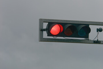 Close-up photo of a red traffic light with a cloudy sky in the background