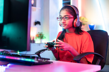 girl kid with wireless headset playing online video game on computer using joystick at home -...