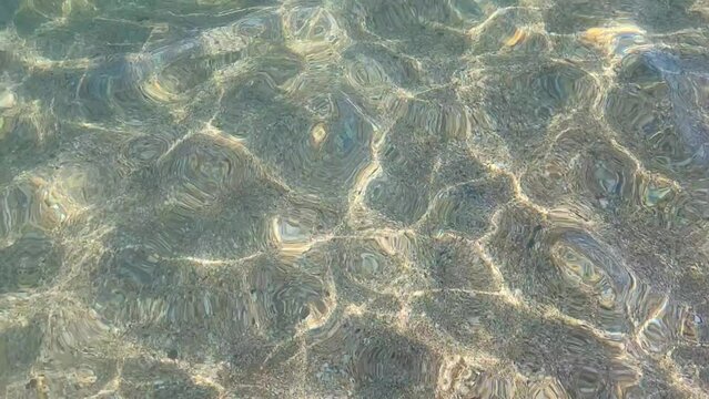 The sun's glare is reflected in the purest transparent sea water close-up, sandy seabed. Small waves run into the water because of the breeze