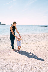 Little boy walks barefoot on a pebble beach holding his mother hands. High quality photo
